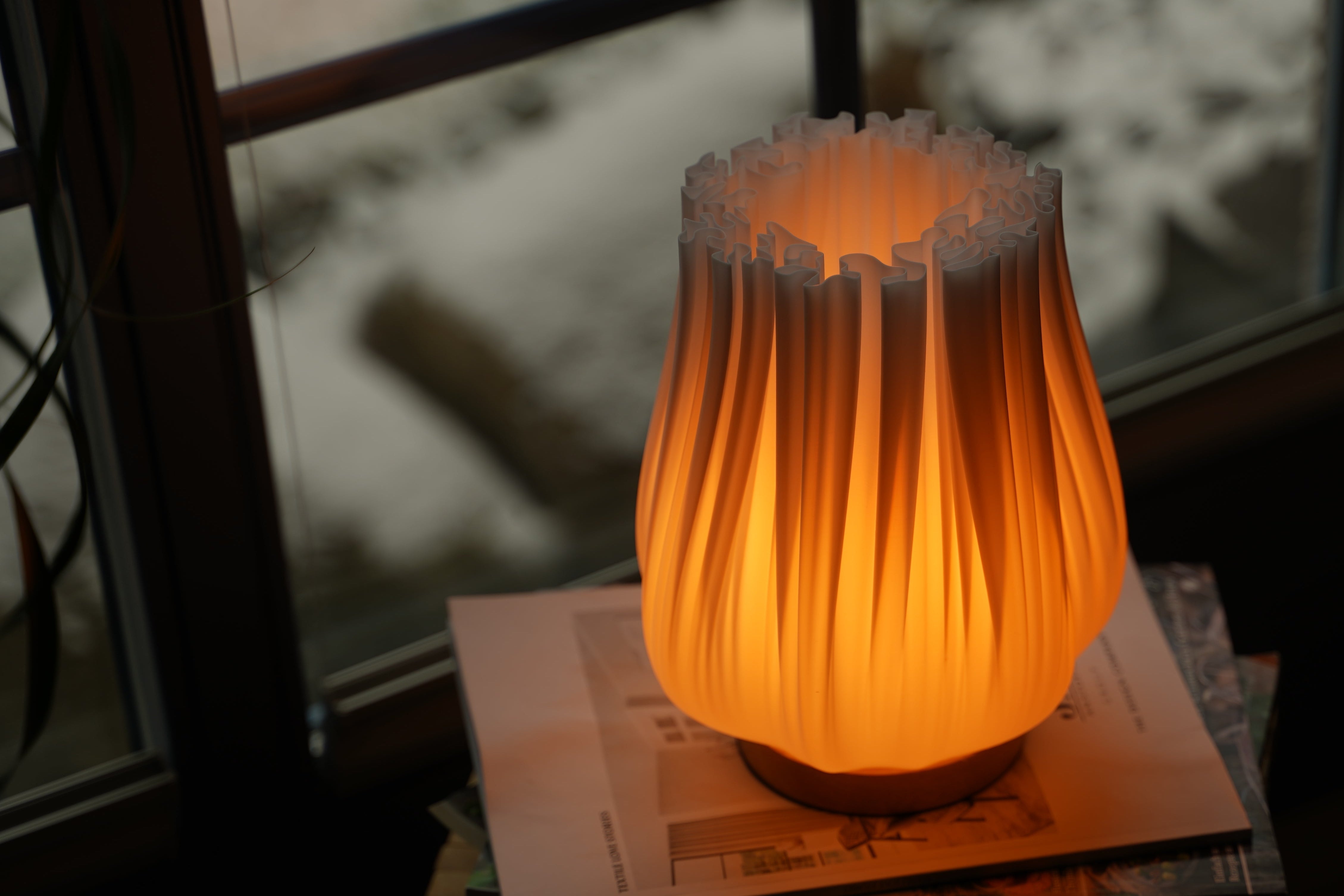 Moonou Finn Tischlampe mit warmem Licht auf einem Buch, vor einem Fenster
